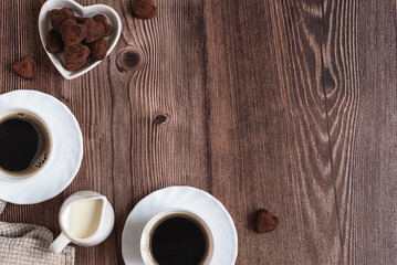Romantic concept for Valentine's Day. Two cups of freshly brewed espresso coffee, a creamer and heart shaped chocolate truffles on a dark wooden table. Morning coffee for two. Place for text.