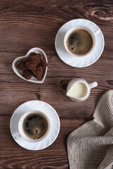 Romantic concept for Valentine's Day. Two cups of freshly brewed espresso coffee, a creamer and heart shaped chocolate truffles on a dark wooden table. Morning coffee for two.