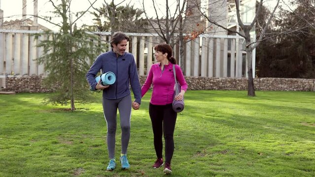 mature couple walking with yoga mats in park