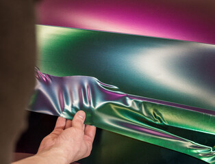 A specialist in wrapping a car with chameleon-colored vinyl film in the process of work. Car wrapping specialists cover the car with vinyl sheet or film. Selective focus.