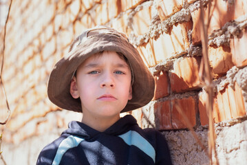 A young small boy of 7-8 years old with a sad look is standing in the shadow of house, boy was...