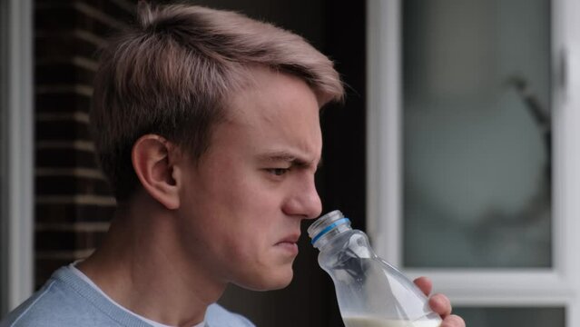 A man sniffs sour milk in a bottle, feeling an unpleasant smell, close-up