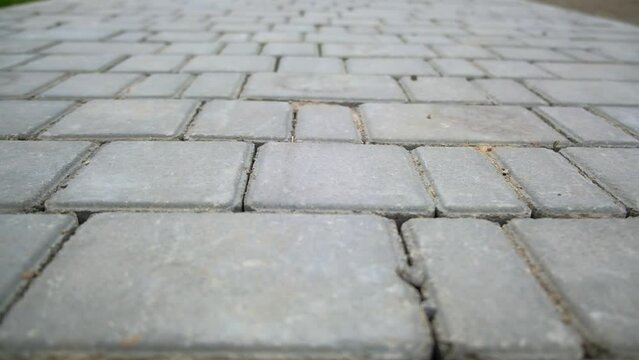 Pavement made of grey brick of diverse size. Going along the concrete paving slabs. Close up.