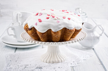 Traditional Russian Easter bread kulich pie with sugar fondant and heart's served as close-up on a white shabby chic cake plate