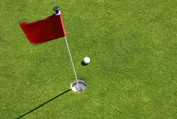 Close up shot of red golf flag and golf ball on golf course putting green shot from above.