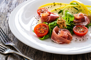 Tasty salad - prosciutto crudo, melon and fresh vegetables on wooden table

