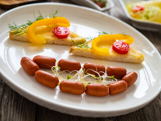 Breakfast - boiled sausages, bread and fresh vegetables served on wooden table
