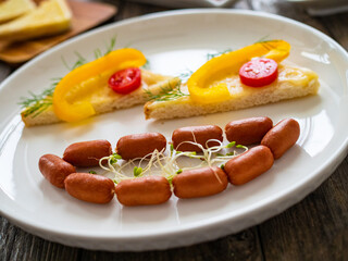 Breakfast - boiled sausages, bread and fresh vegetables served on wooden table

