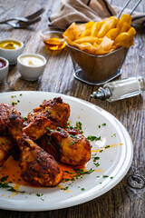 Barbecue chicken drumsticks with French fries on wooden table
