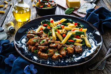 Pasta with roasted pork loin, spinach and parmesan on wooden table
