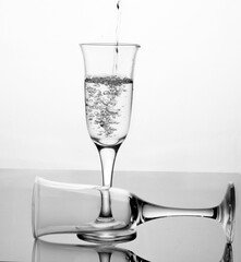 Water is poured into a glass on a glass table with reflection