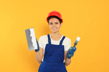 Professional worker with putty knives in hard hat on orange background