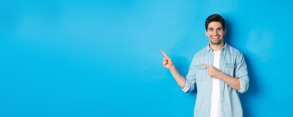 Handsome caucasian man in casual outfit, pointing fingers left and smiling, showing promo offer,...