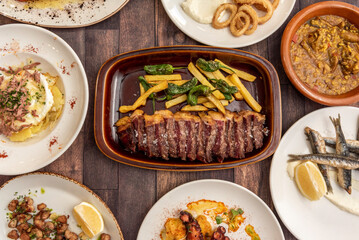 Set of dishes and tapas of Spanish gastronomy with sliced grilled beef entrecote with french fries,...