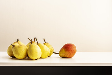 A bunch of delicious ripe yellow pears and one different pear seen from above on a white table and a white wall in the background