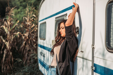 Beautiful brunette girl leaning on a camp trailer with hands in the air