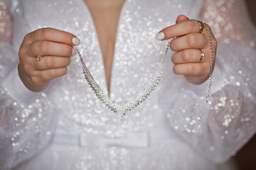An expensive necklace in the hands of the bride on the background of a wedding dress 4347.