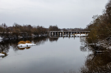 Wooden bridge over the river in winter on which cars drive. An unfrozen river in winter due to warm weather.
