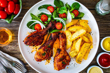 Barbecue chicken drumsticks with french fries, lettuce and mini tomatoes on wooden table
