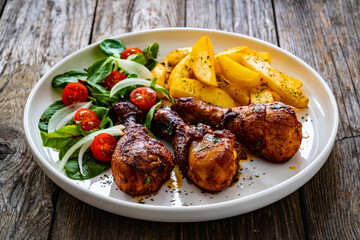 Barbecue chicken drumsticks with french fries, lettuce and mini tomatoes on wooden table
