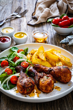Barbecue chicken drumsticks with french fries, lettuce and mini tomatoes on wooden table
