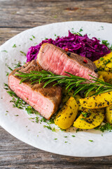 Fried beef sirloin with potatoes and reg cabbage salad on wooden table
