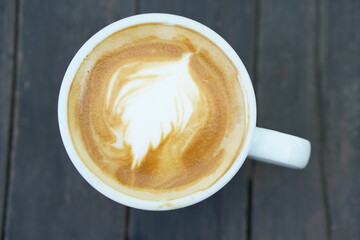 Hot coffee with floral foam in a white cup gray wood background