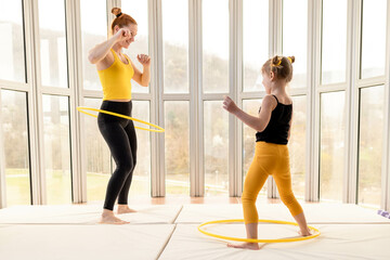 Young fit mom and her daughter having fun with hula hoop in a gym