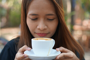 Asian woman inhaling aromatic coffee