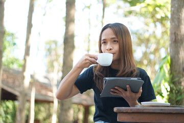 Asian women are happy to sit and work in a coffee shop. There are green trees surrounded by nature.