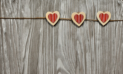 Three red hearts in the form of clothespins attached to a jute rope, on a gray rustic table, love and romance, a background idea for Valentine's day. Top view. Background with space to copy.