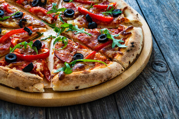 Circle pizza nduja with mozzarella, black olives and arugula leaves on wooden table
