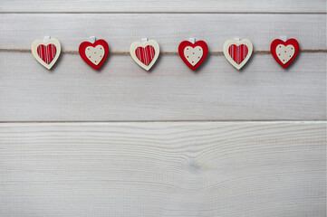 Wooden love hearts suspended from a rustic rope on a white wooden background. Valentine's Day greeting card. Space for copying.