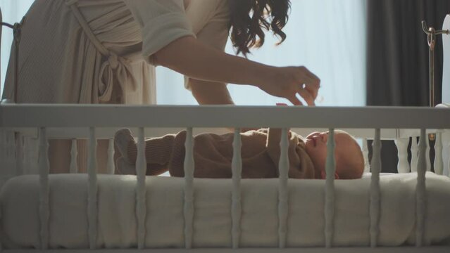Side view of a little cute baby lying in the crib and mother putting a pacifier in baby's mouth. Shot in slow-motion