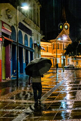 Homem caminha solitário com guarda-chuva em noite de intensa chuva na região da Estação Cultura.