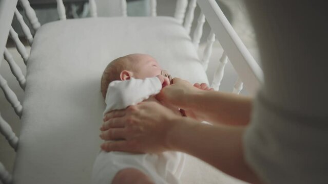 Little newborn baby sleeping in the white wooden crib and sucking a pacifier while mother holding the baby. Shot in slow-motion