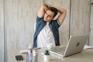 young man stretching at work while sitting at desk having back pain