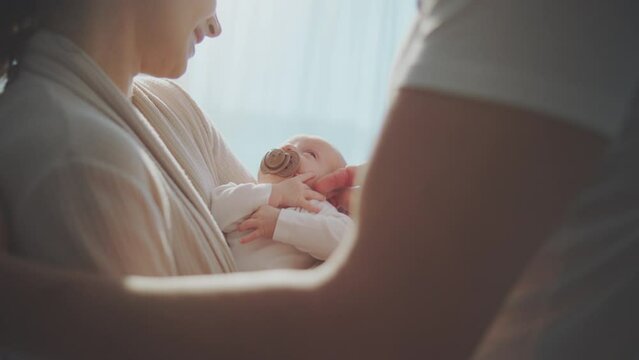 Close-up portrait of happy smiling mother and father with their baby boy. Parents caring baby with a pacifier in mouth. Shot in slow-motion