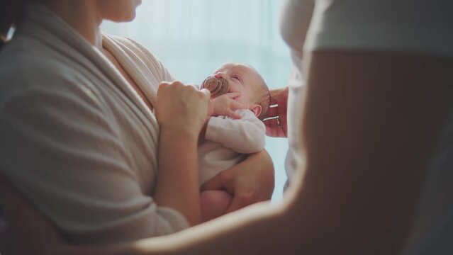 Portrait of caucasian smiling mother and father caring newborn baby with pacifier in mouth. Loving parents enjoying caring little child in slow-motion