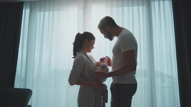 Slow-motion shot of young father and mother holding baby on hands, caressing their cute newborn baby daughter. Parents expressing unconditional love