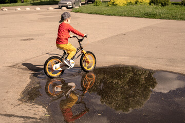happy boy rides a tricycle in a puddle on a walk.