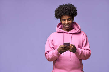 Young happy cool curly African American teen guy wearing pink hoodie holding cell phone using mobile digital apps on cellphone technology texting on smartphone isolated on light purple background. - obrazy, fototapety, plakaty