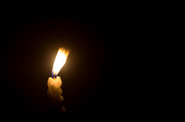 Blurred photo of single burning candle flame or light glowing on a spiral white candle against...