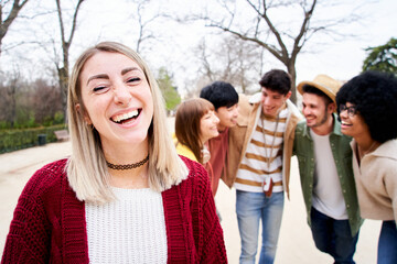 Young smiling girl looking at the camera outdoors with group of friends. Happy people having fun together Focus on a pretty young woman. University Colleagues at campus. High quality photo