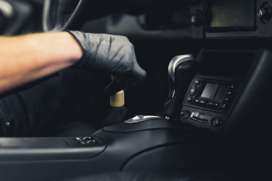Close-up shot ot male hand in black glove inside car brushing gear shift. Precision work. Car interior detailing concept. Horizontal indoor shot. High quality photo