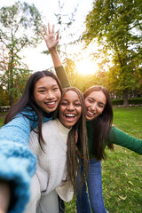 Vertical Portrait of three girls outside having fun taking selfie. An Asian Chinese woman, a black...