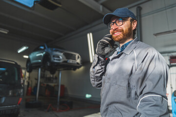 A car mechanic in a grey jacket at an auto repair shop with lifted cars for repair. High-quality photo