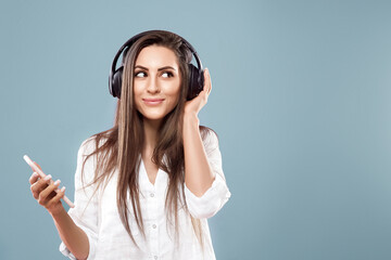 Beautiful woman listening to music using wireless headphones in studio isolated over blue...