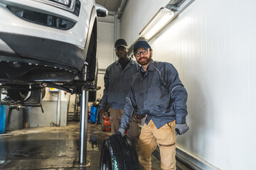 Fototapeta na wymiar Car mechanics near a lifted white luxury car replacing wheels in a repair station. High-quality photo