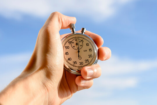 Cropped hand of man holding stopwatch against sky